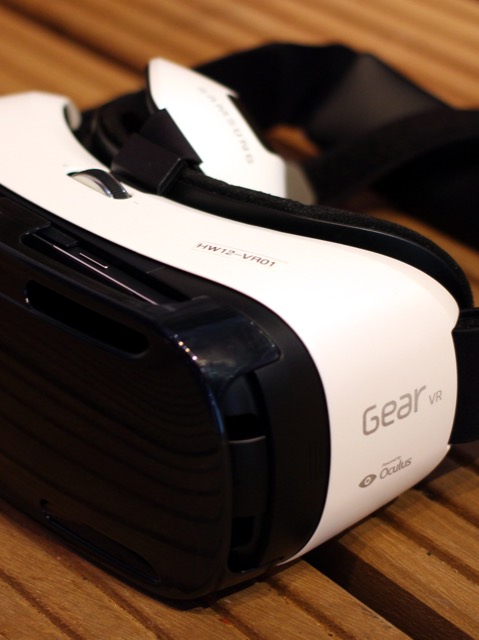 Samsung Gear VR : photographie du casque de réalité virtuelle mobile, coque blanche et sangles noires, posé sur une table en bois.